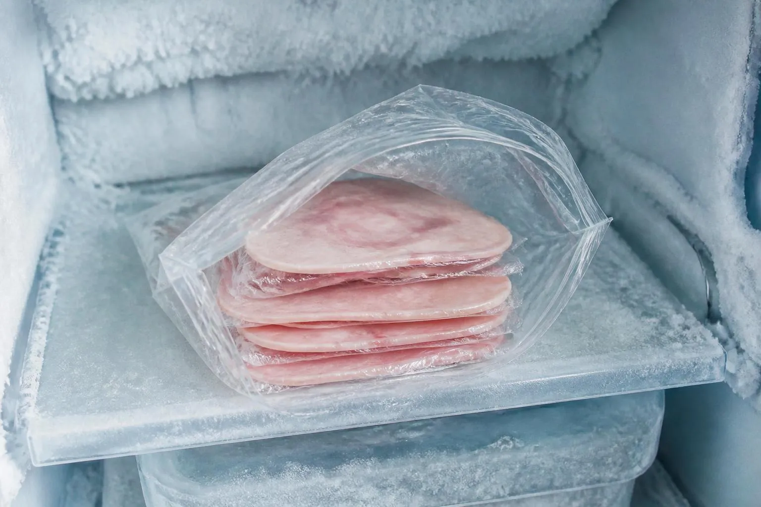 Des tranches de jambon blanc séparées par du film alimentaire dans un sachet de congélation, posées sur une clayette givrée