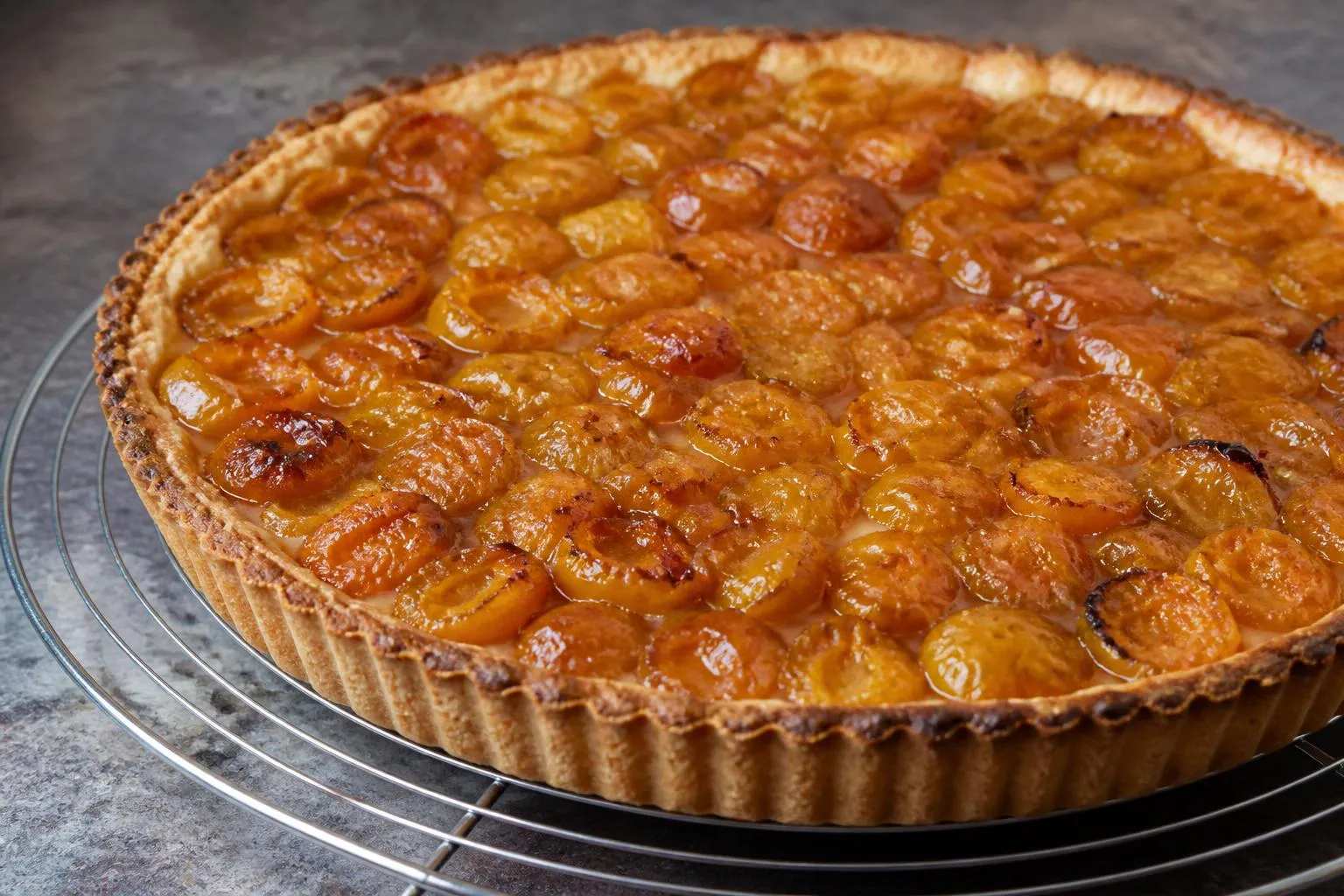 Une tarte aux mirabelles dorée posée sur une grille à la sortie du four, le jus épaissi entre les fruits
